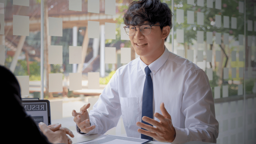 مرشح حديث التخرج يرتدي قميصاً وربطة عنق بيضاء يجري مقابلة عمل، مع انعكاس السيرة الذاتية (Resume) على الشاشة أمامه.