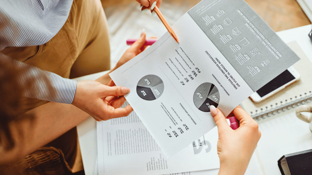 لقطة قريبة تظهر شخصين يعملان على تحليل بيانات ورسوم بيانية دائرية (Pie Charts) في تقرير، ترمز إلى التحليل المالي واتخاذ القرارات الإدارية.