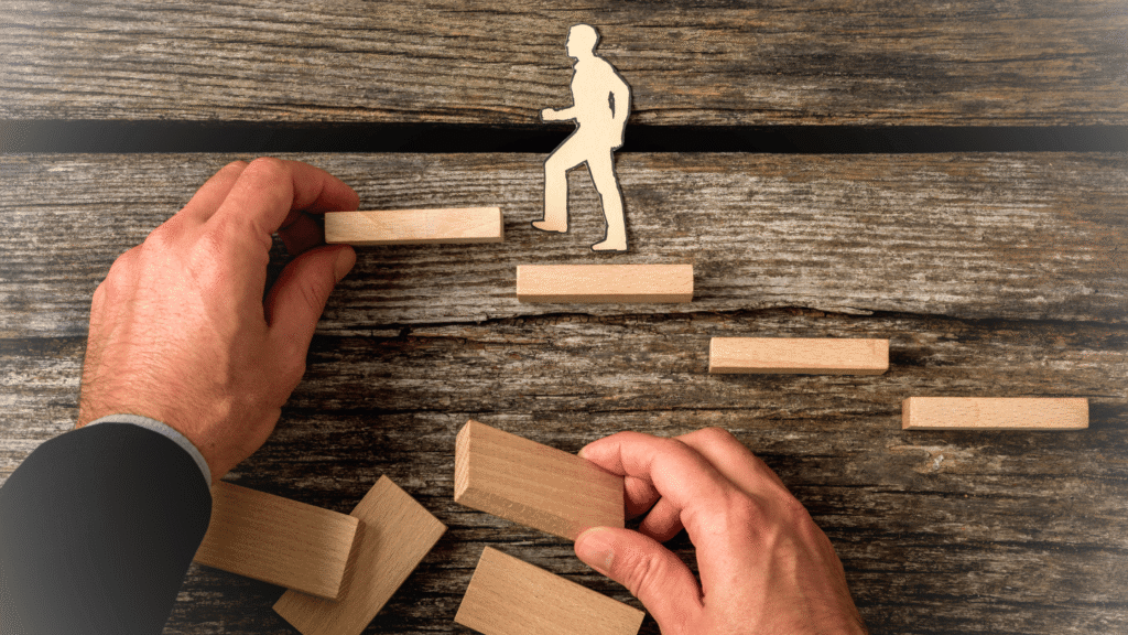 أيادٍ تبني سلّمًا من كتل خشبية، ترمز إلى التطوير المهني ووضع خطة الترقية والتطور في العمل خطوة بخطوة. يجسد بناء الأساس لطلب ترقية ناجح.