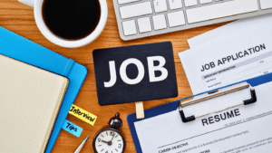 سيرة ذاتية (Resume) واستمارة طلب وظيفة (Job Application) موضوعة على مكتب مع كلمة JOB بارزة. يمثل كيفية تطبيق هدف وظيفي جاهز لحديثي التخرج في طلبات العمل.