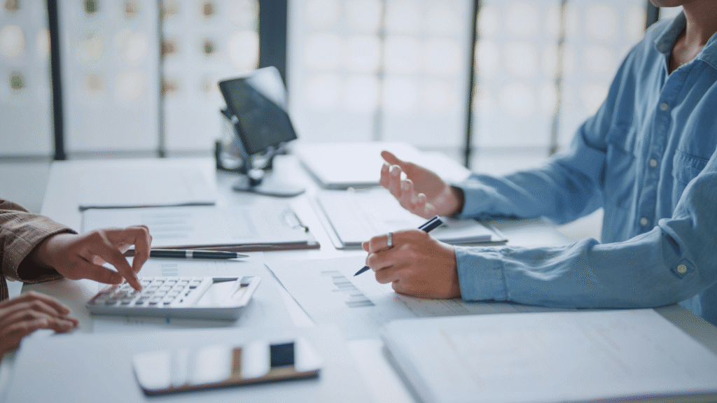 اجتماع عمل بين موظفين لمراجعة التقارير المالية وتحليل الرواتب باستخدام الحاسبة، تخطيط إداري واتخاذ قرارات مهنية داخل شركة